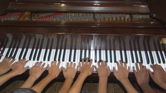 Multiple hands playing on a piano keyboard