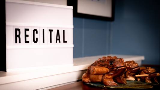Lightbox with 'RECITAL' text next to a wooden frog sculpture on a shelf.