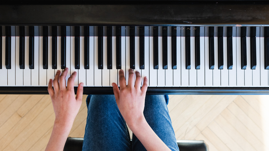 Close-up of hands playing a piano keyboard on a wooden floor.