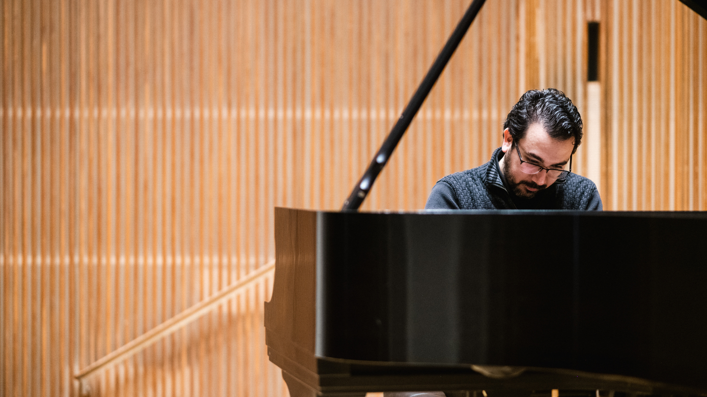 Man playing a grand piano in a room with wooden paneling