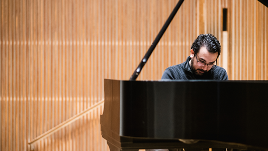 Man playing a grand piano in a room with wooden paneling