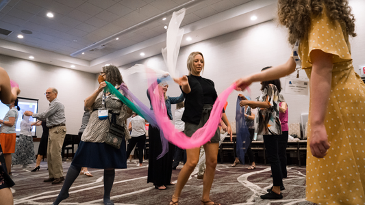Group of people participating in a team-building activity with colorful ribbons in a conference room.