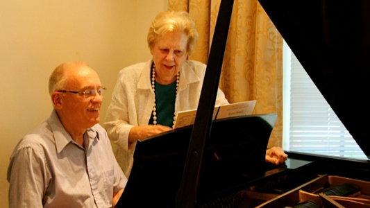 Two elderly people playing a piano together.