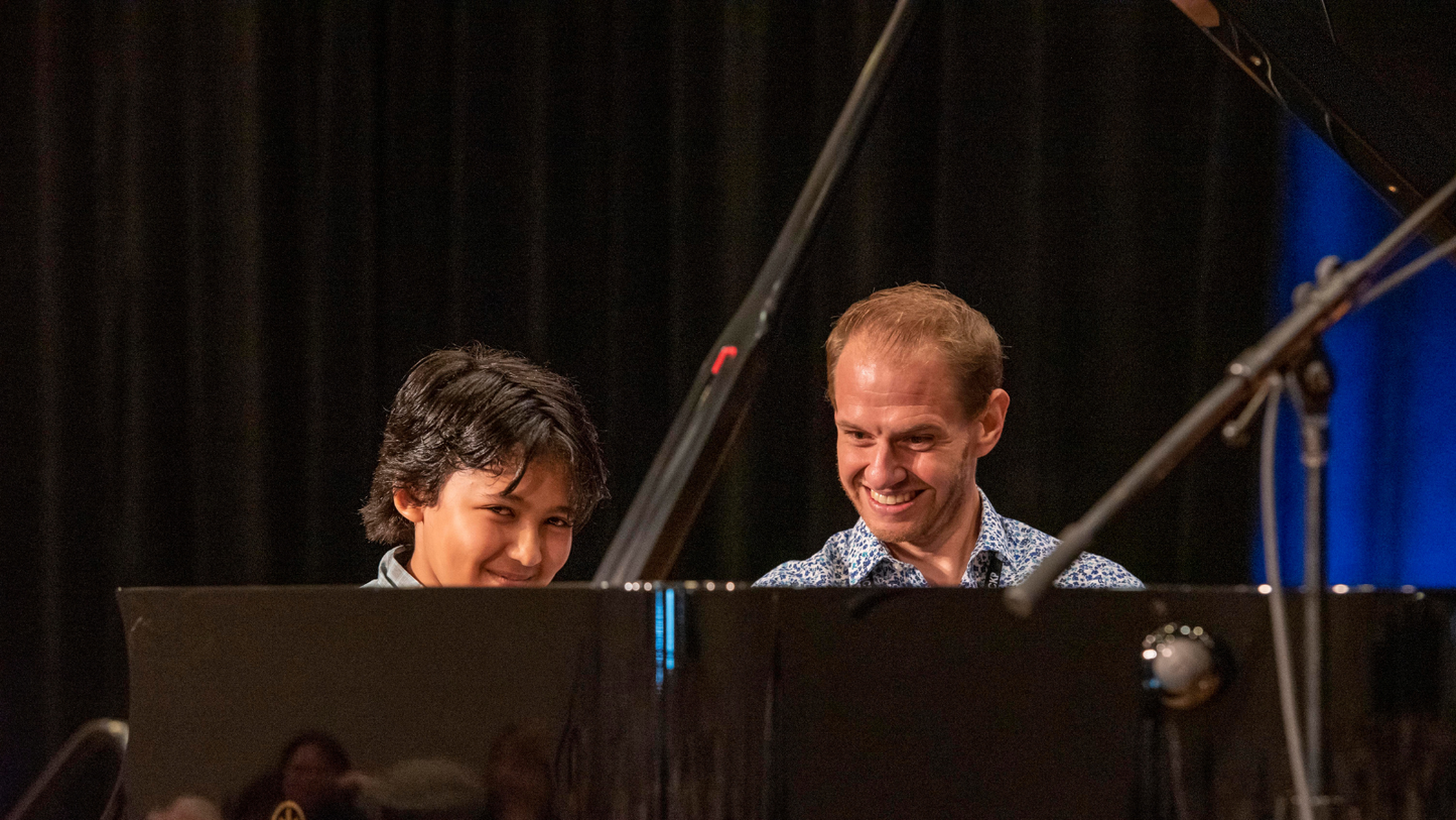 Two musicians playing piano on a stage with a dark curtain background