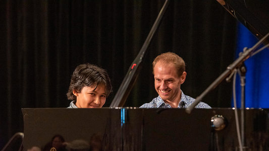 Two musicians playing piano on a stage with a dark curtain background